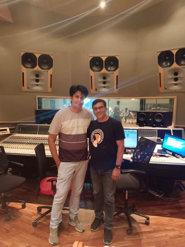 Aslam Keyi with a collaborator at a large mixing console, orchestra visible through the studio glass