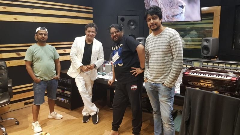 Four collaborators standing in a wood-panelled recording studio