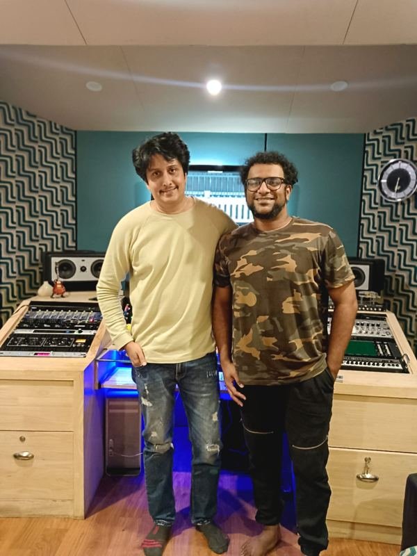 Two collaborators standing at a mixing desk in a blue-lit studio